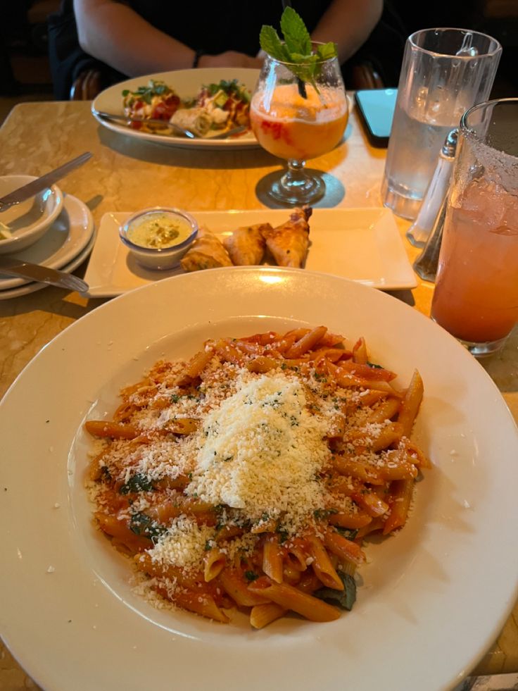 a white plate topped with pasta covered in parmesan cheese next to a glass of orange juice