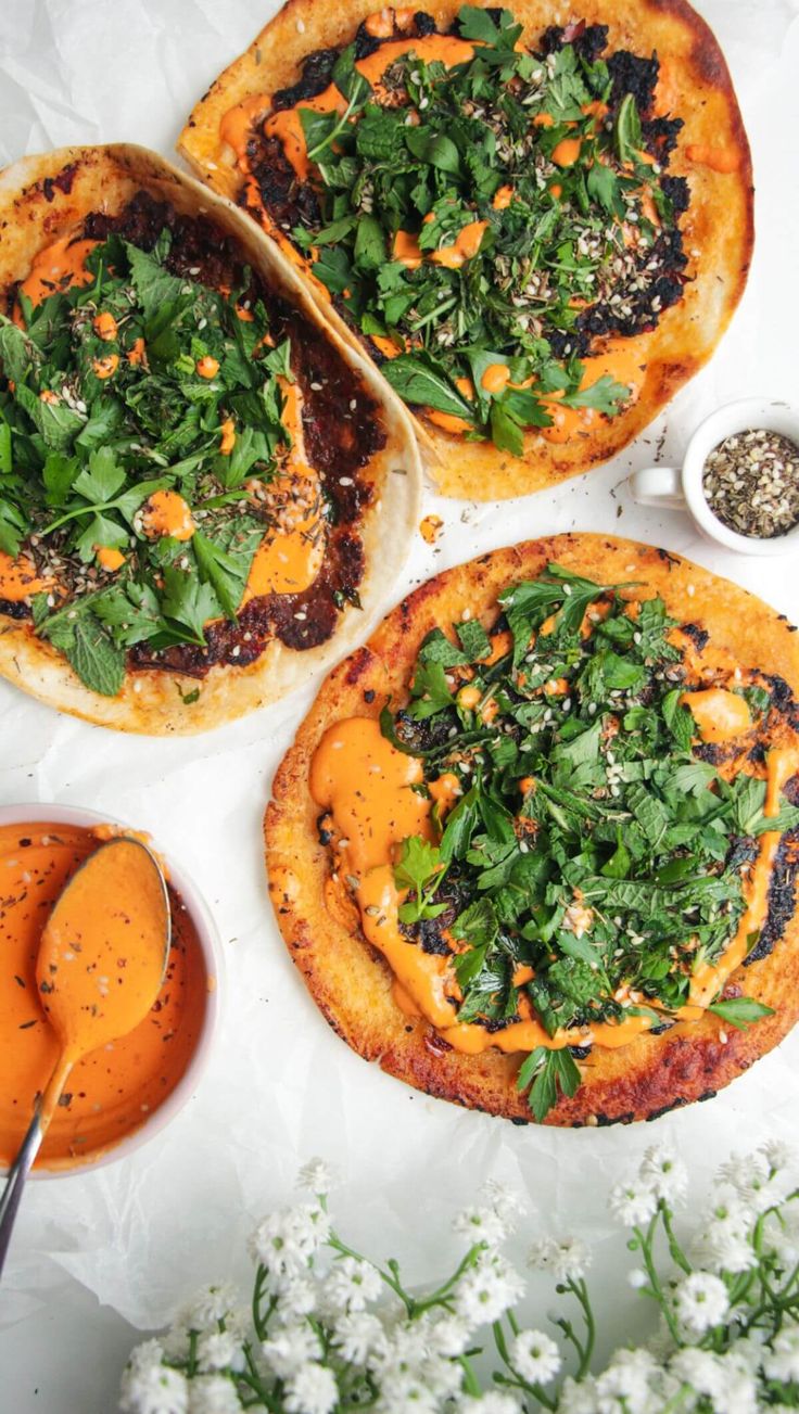 three pizzas with different toppings on top of them next to sauce and flowers