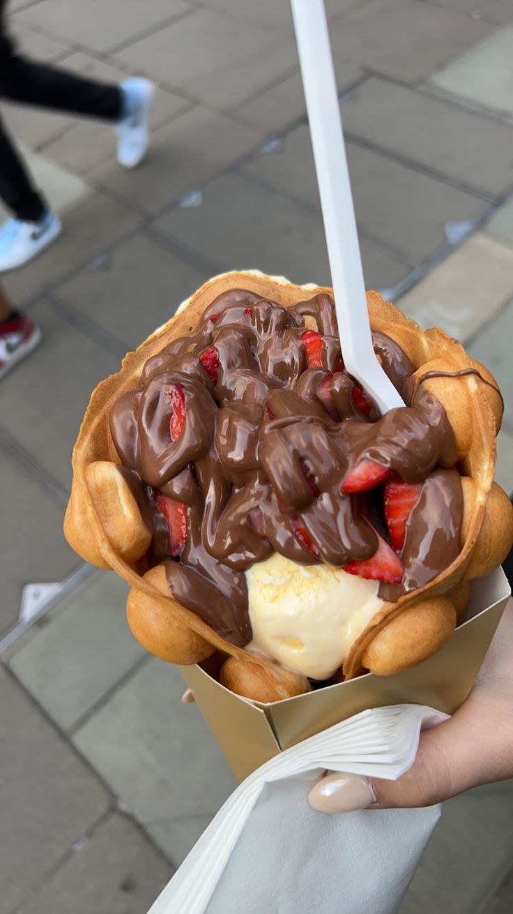 a person holding a waffle with chocolate and strawberries in it on the street