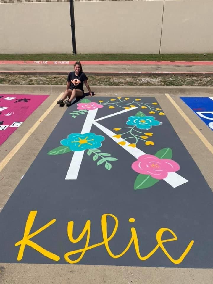 a woman sitting on the ground in front of a parking lot with flowers painted on it