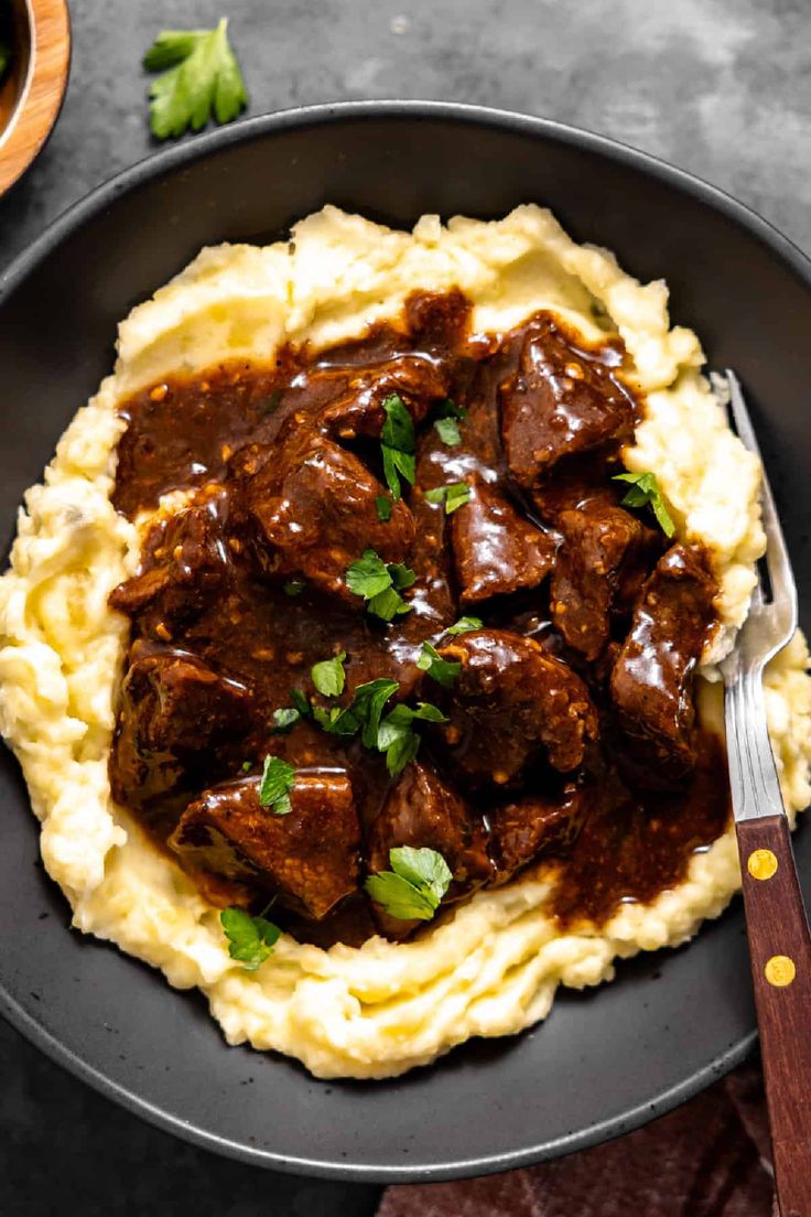 a black plate topped with mashed potatoes and beef