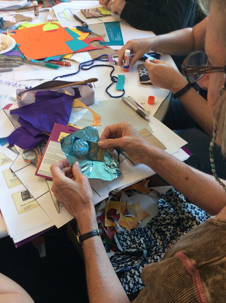 two people working on crafts at a table with papers and scissors in front of them