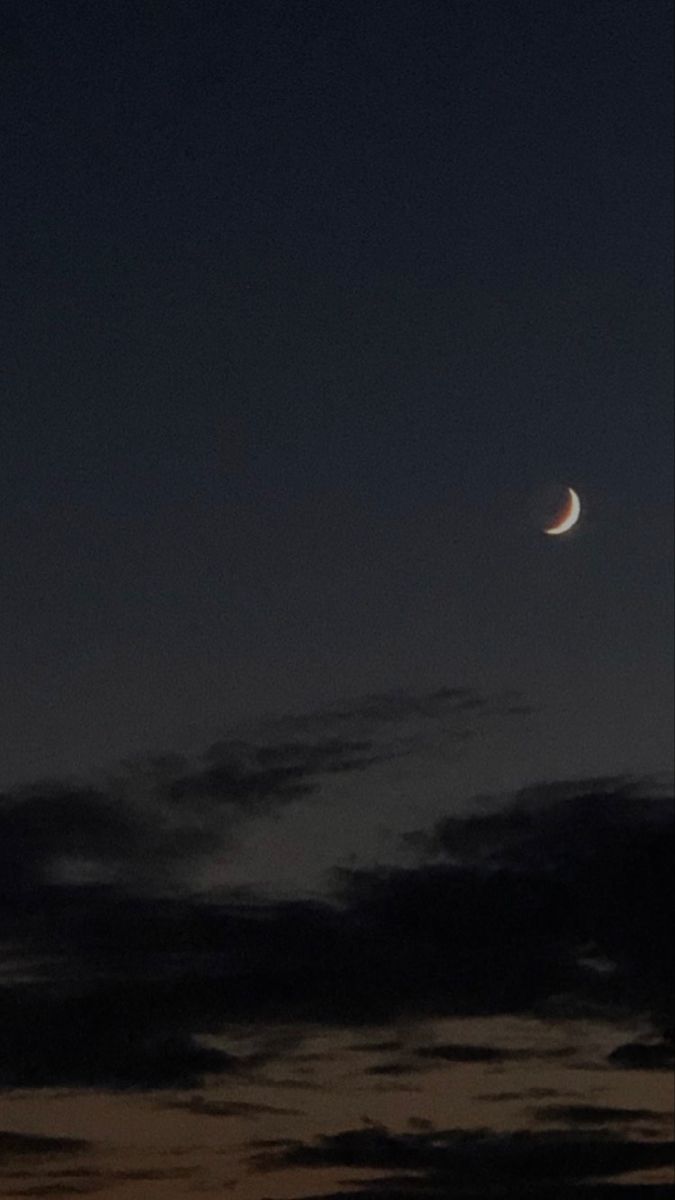 the moon is seen in the night sky with clouds and dark blue skies behind it