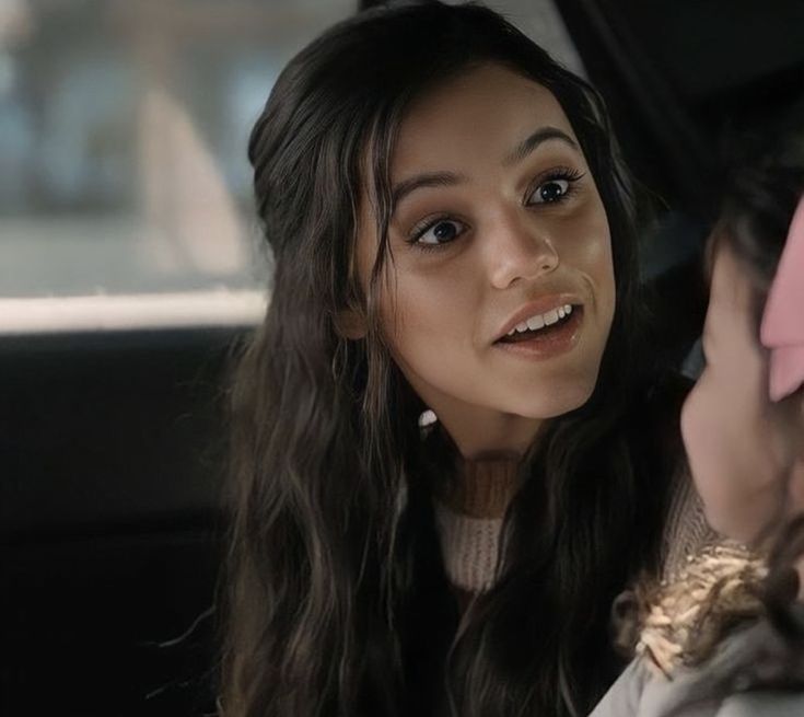 a woman sitting in the back seat of a car talking to another woman who is looking at her