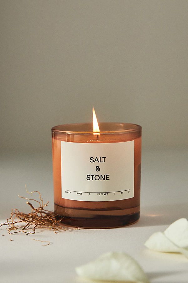 a candle sitting on top of a table next to some white flower petals and leaves