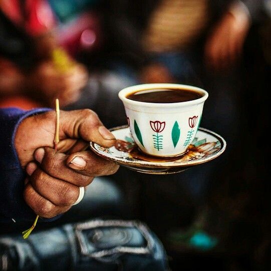 a person holding a coffee cup and saucer with a spoon in their left hand