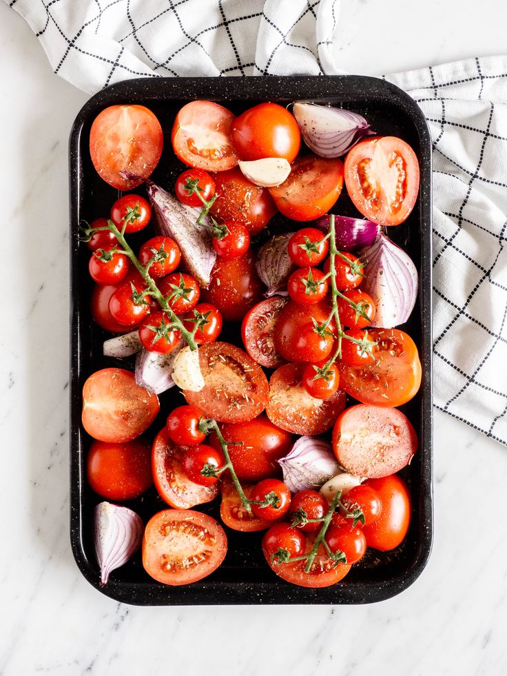 tomatoes, onions and garlic on a black tray with a white towel in the background