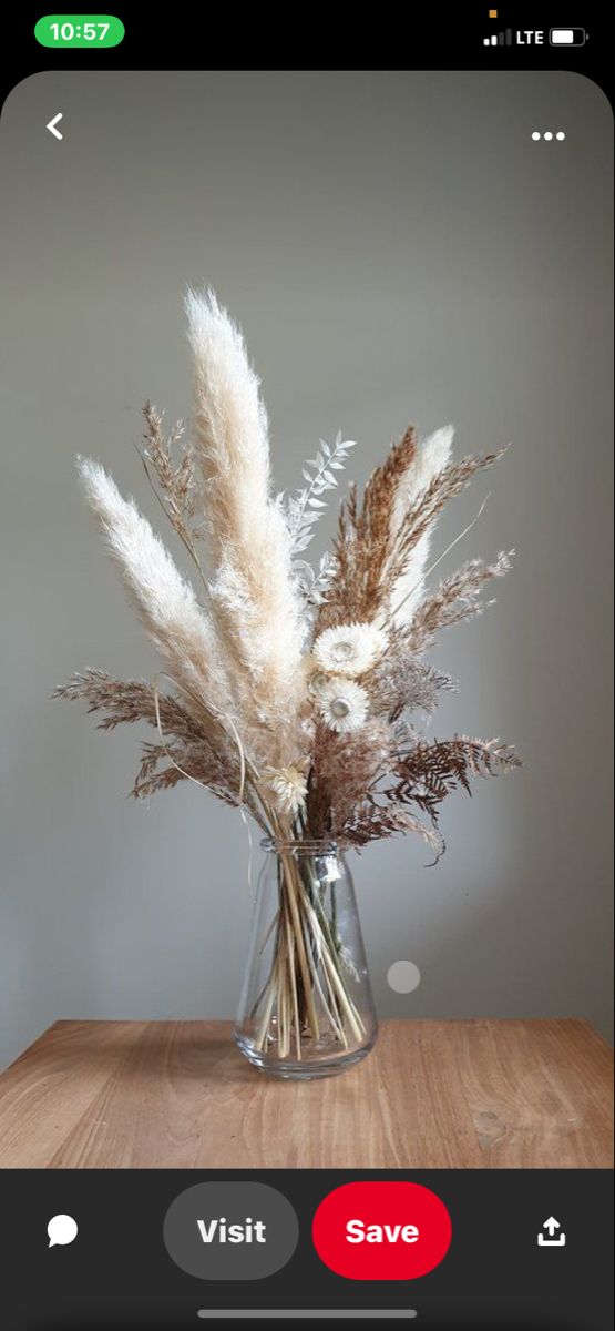 a glass vase filled with dried flowers on top of a wooden table