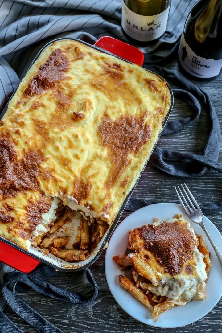 a casserole dish with meat and cheese next to a bottle of wine