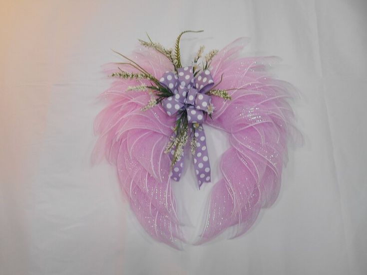 a pink and purple feather wreath with polka dots on the front, attached to a white wall