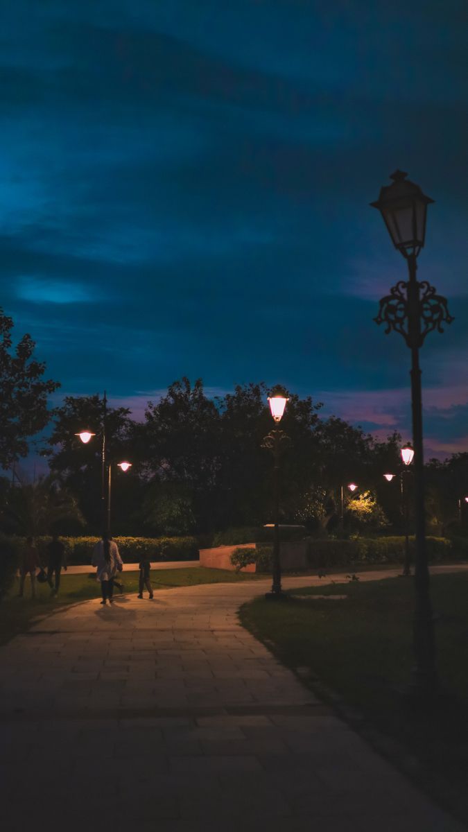 people walking down a path at night with street lamps on either side and dark clouds in the sky