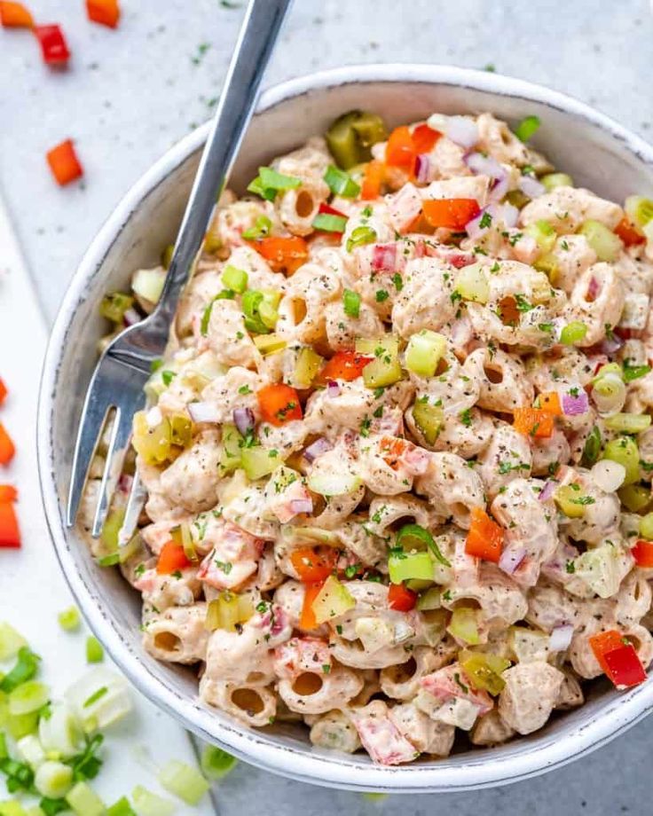 a bowl filled with pasta salad next to sliced carrots and celery on the side