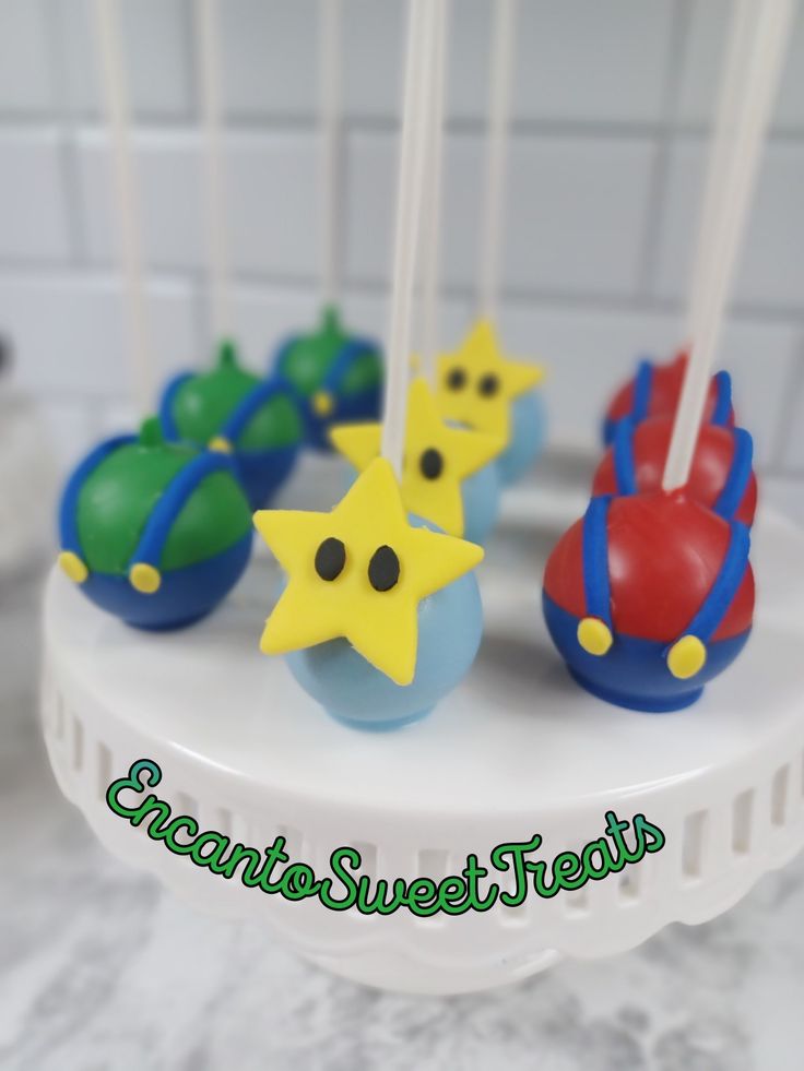 cake pops decorated with stars and shapes on top of a white plate in front of a tiled wall