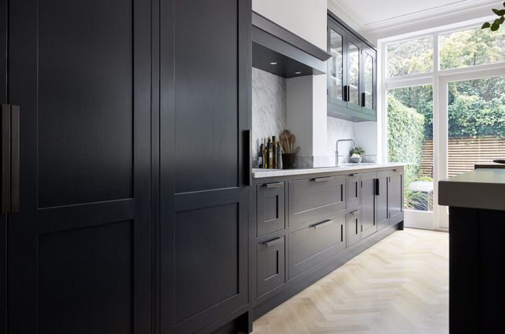 a kitchen with black cabinets and white counter tops next to a large window that looks out onto the backyard