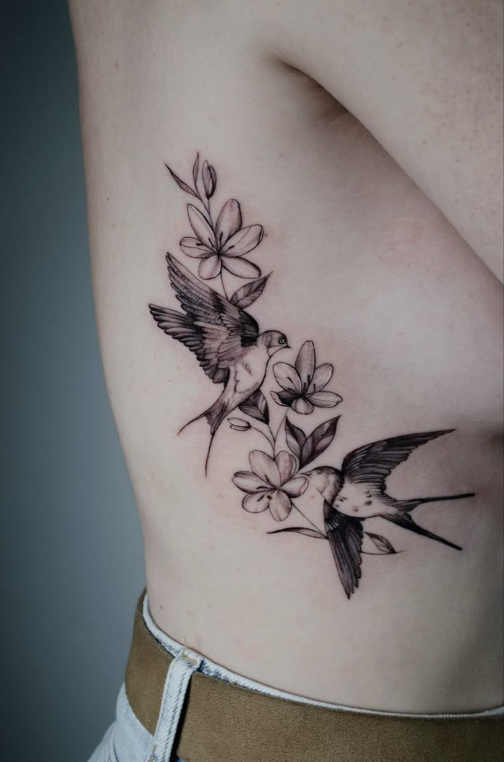 a woman's stomach with flowers and birds tattoo on her side, showing the breast area