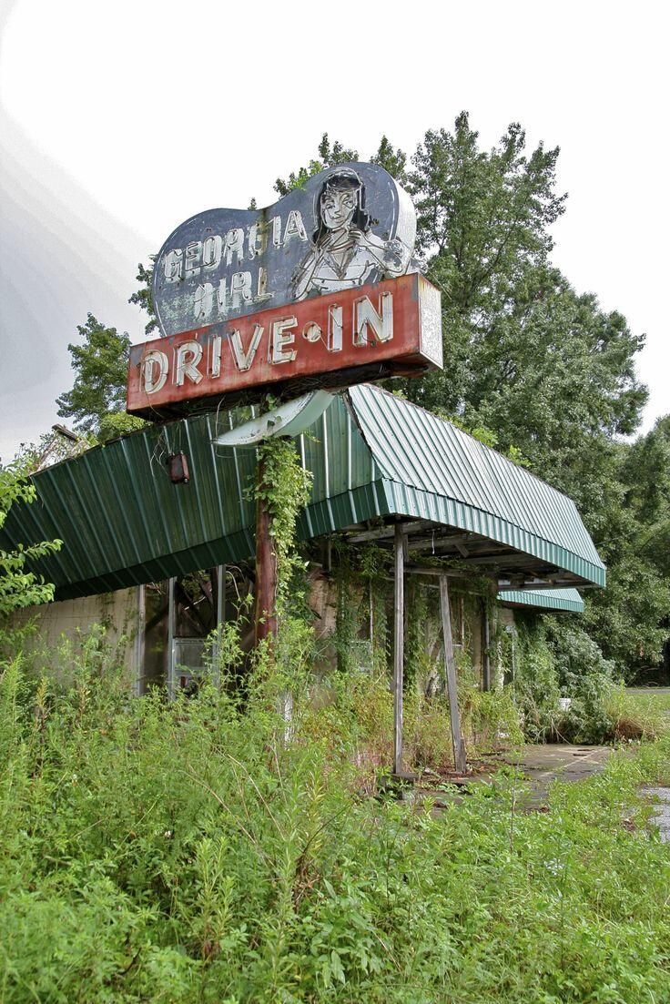 an old drive - in movie theater sitting on the side of a road with overgrown vegetation