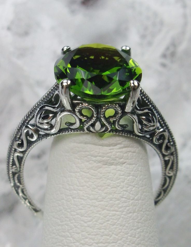 Natural Peridot Ring Swan Design#190 Custom Here we have an Art Deco inspired ring in 10k white gold, 14k white gold or solid sterling silver filigree with a Natural green peridot gemstone. This full cut oval cut 5ct peridot is 12mm in length and 10mm in width. The setting is 12mm NS on the finger. The inside of the band is marked 10k, 14k, or 925 for sterling (by choice). Notice the beautiful etched design of the silver filigree setting. A gift ring box is included and all rings are shipped in Green Filigree Ring For Anniversary, Green Emerald Ring With Intricate Design, Intricate Design Round Emerald Anniversary Ring, Intricate Emerald Anniversary Ring, Intricate Round Emerald Anniversary Ring, Green Gemstone Filigree Ring For May Birthstone, Intricate Design Emerald Anniversary Ring, Green Gemstone Filigree Ring, Green Oval Emerald Ring With Intricate Design