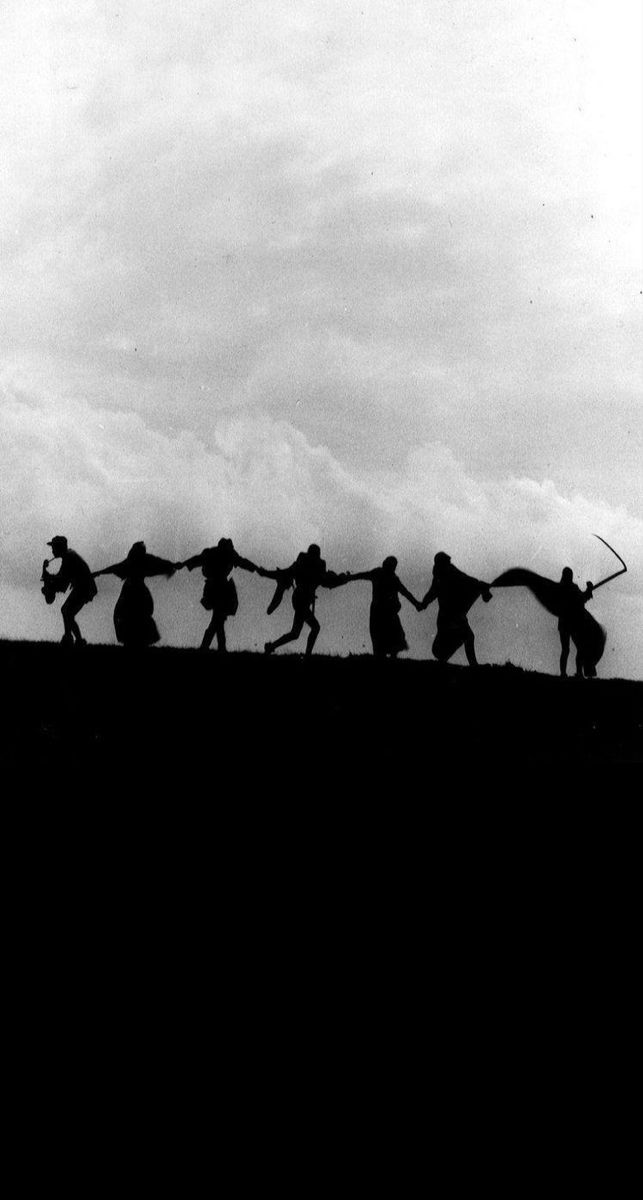 black and white photograph of people holding hands on top of a hill with clouds in the background