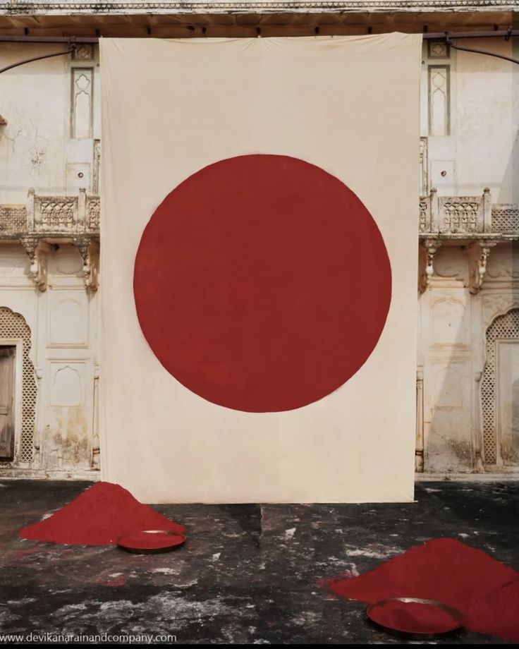 a large red and white painting in front of an old building with no one around it