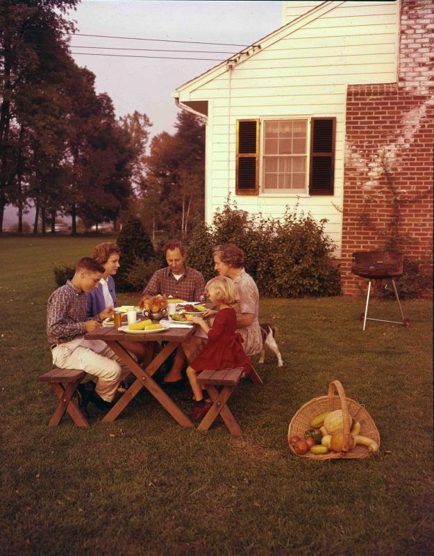 a group of people sitting around a table eating food on top of a grass covered field