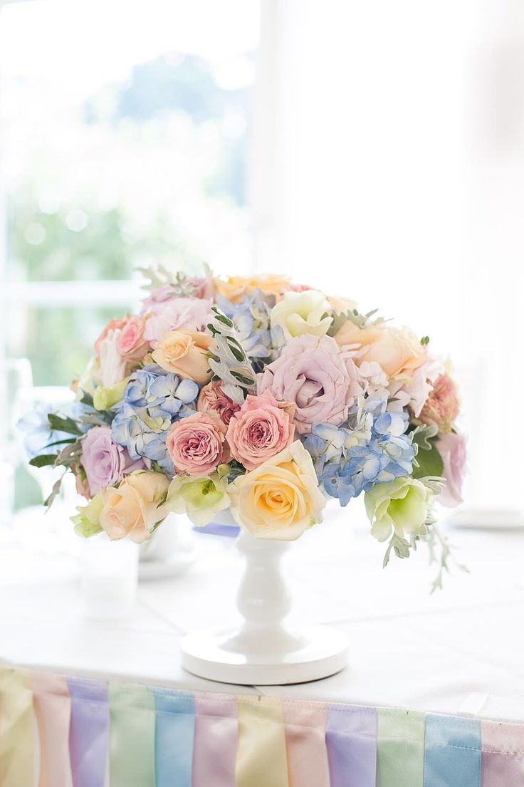 a white vase filled with colorful flowers on top of a striped tablecloth covered table