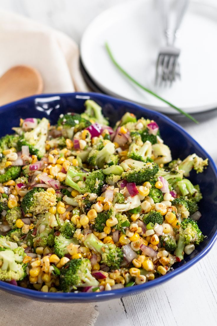 a blue bowl filled with corn and broccoli on top of a white table