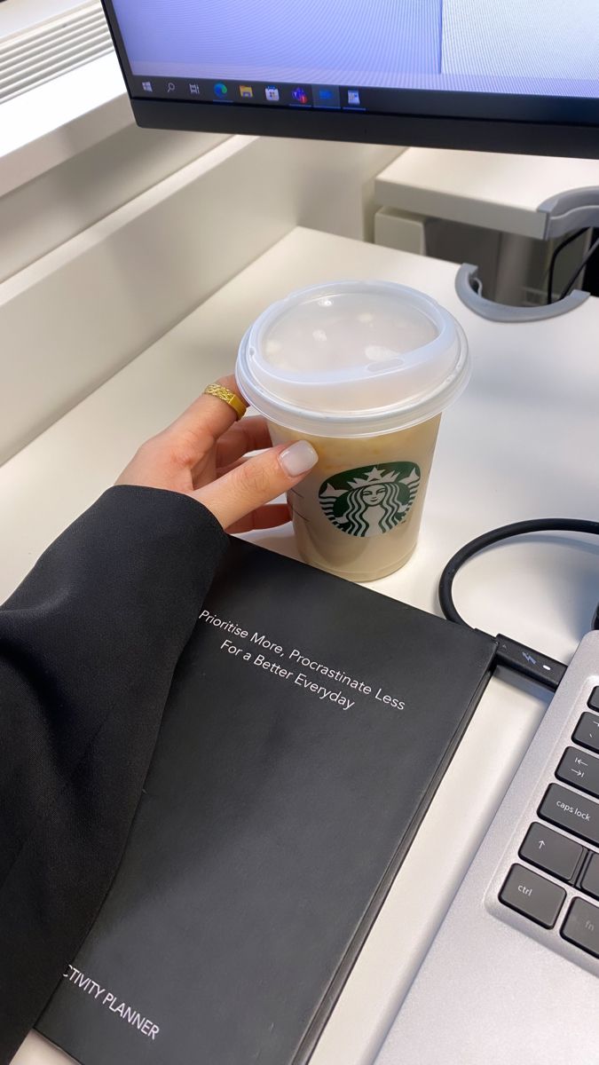 a person is holding a starbucks cup in front of a computer keyboard and book on a desk