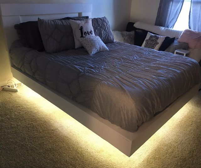 a bed with pillows and lights on the headboard is lit up in front of a window