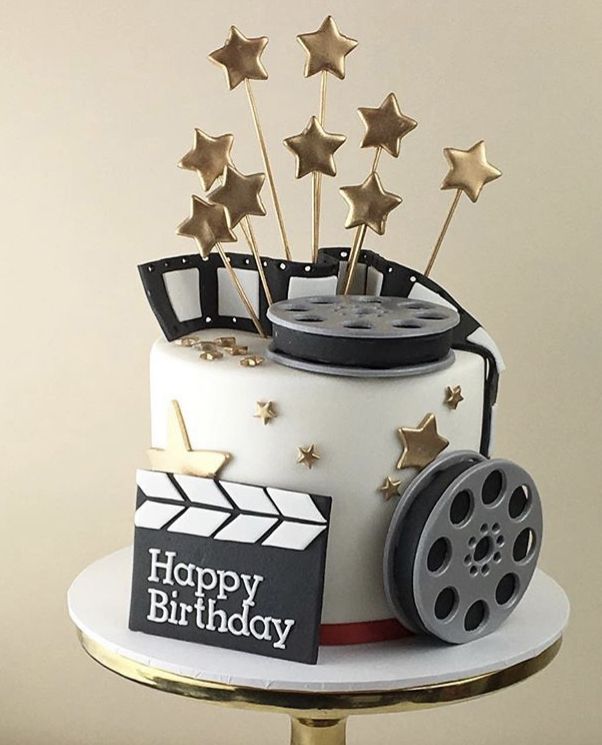 a birthday cake decorated with gold stars and a film reel on the top, sitting on a table