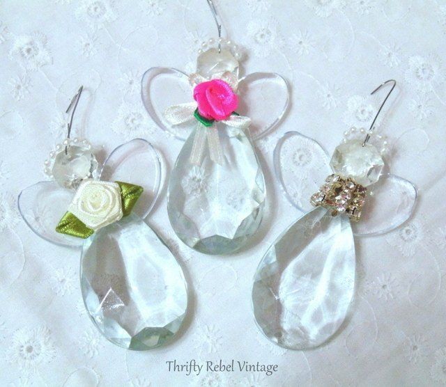 three glass angel ornaments with flowers and pearls on white lace background, one pink rose in the center