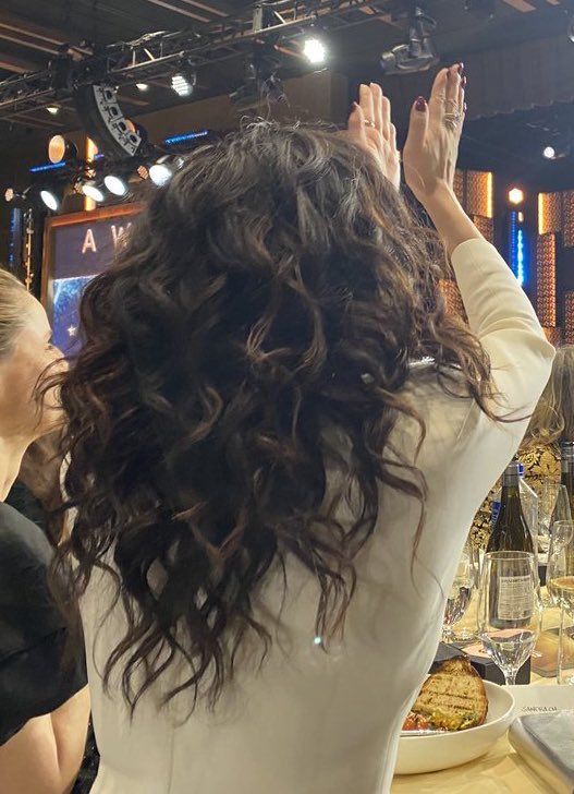 a woman with her hands up in the air at a table full of food and wine glasses