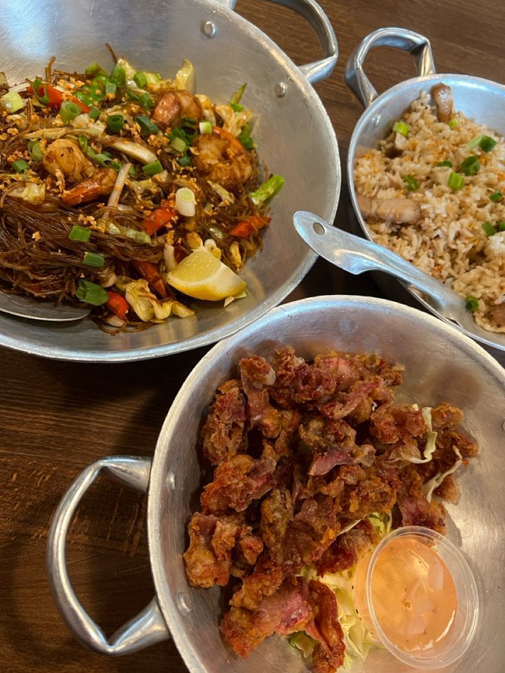 three metal pans filled with food on top of a wooden table next to each other