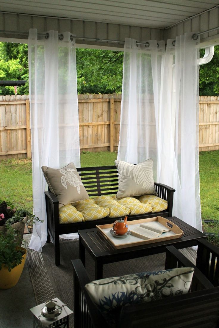 an outdoor living area with couches, tables and curtains on the side of it