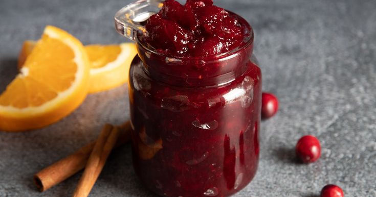 a glass jar filled with cranberry sauce next to an orange and cinnamon stick