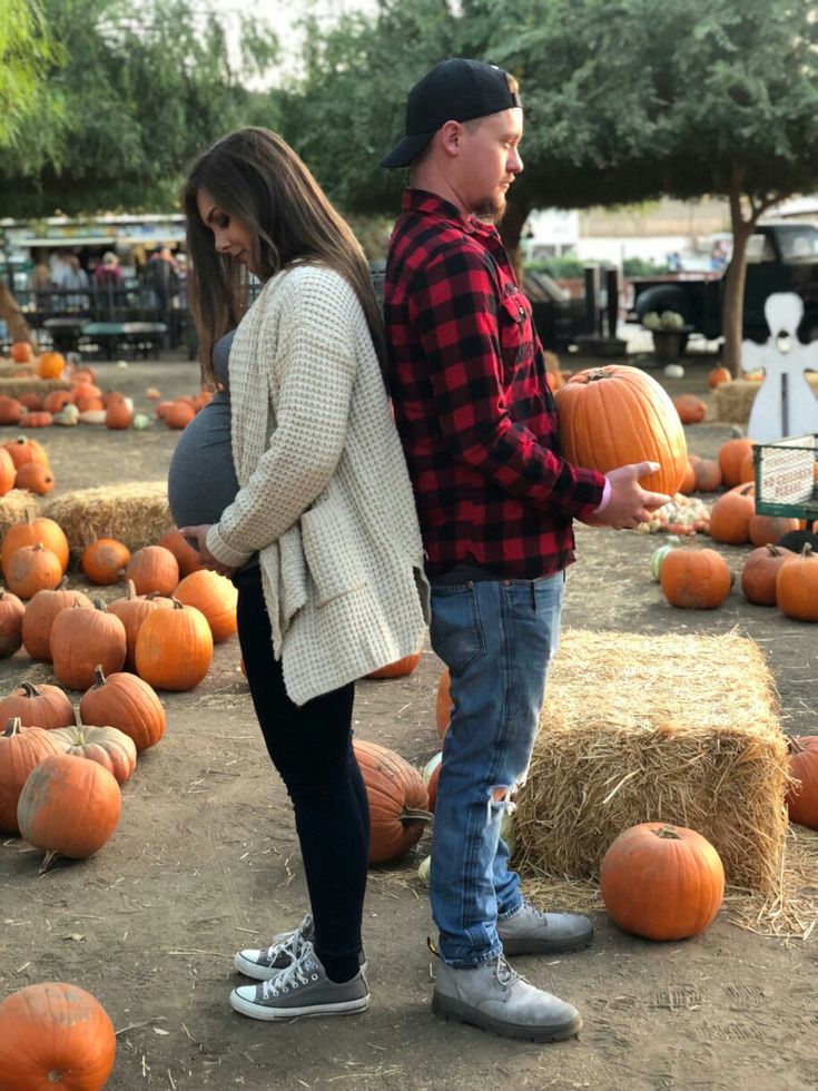 a man and woman standing next to each other in front of pumpkins