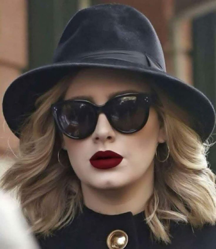 a woman wearing sunglasses and a hat with red lipstick on her lips is walking down the street