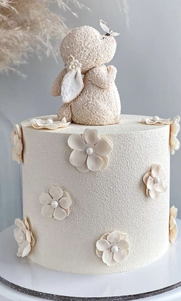 a white cake decorated with flowers and a teddy bear figurine sitting on top