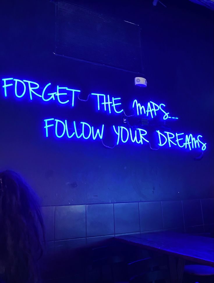 a neon sign that reads forget the maps, follow your dreams on a wall in a restaurant