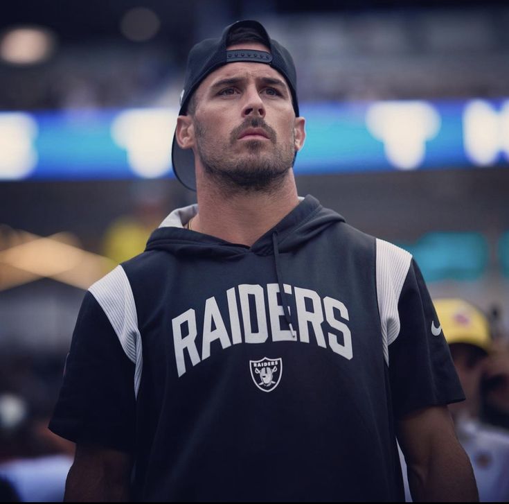 a man wearing a oakland football hoodie looks up at the sky in an arena