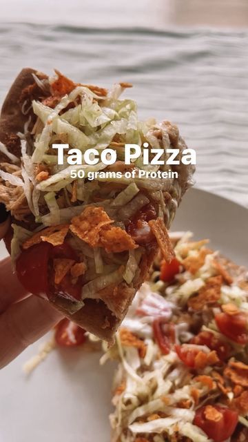 a hand holding a piece of taco pizza on top of a white plate