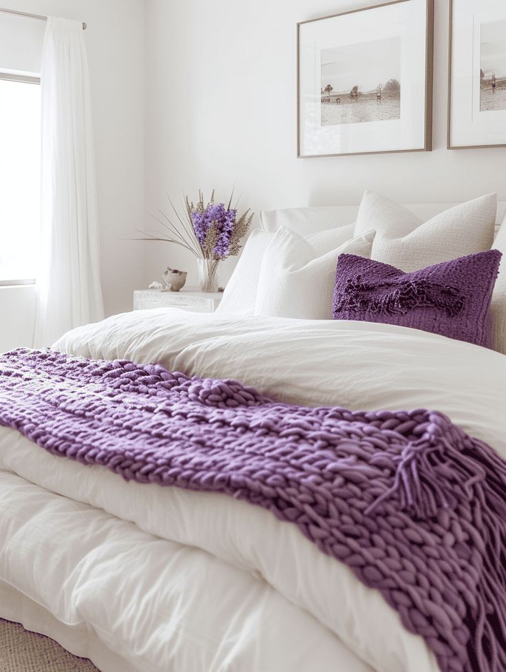 a white bed topped with purple pillows and blankets