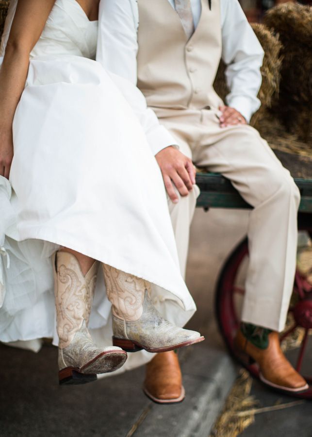 a bride and groom are sitting on a bench in their wedding attire with cowboy boots