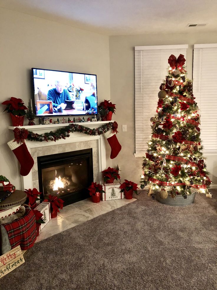 a living room decorated for christmas with a fireplace and tv in the corner, stockings on the mantel