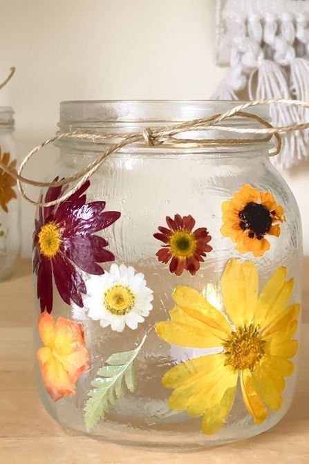 a jar with flowers painted on it sitting on a table next to two mason jars