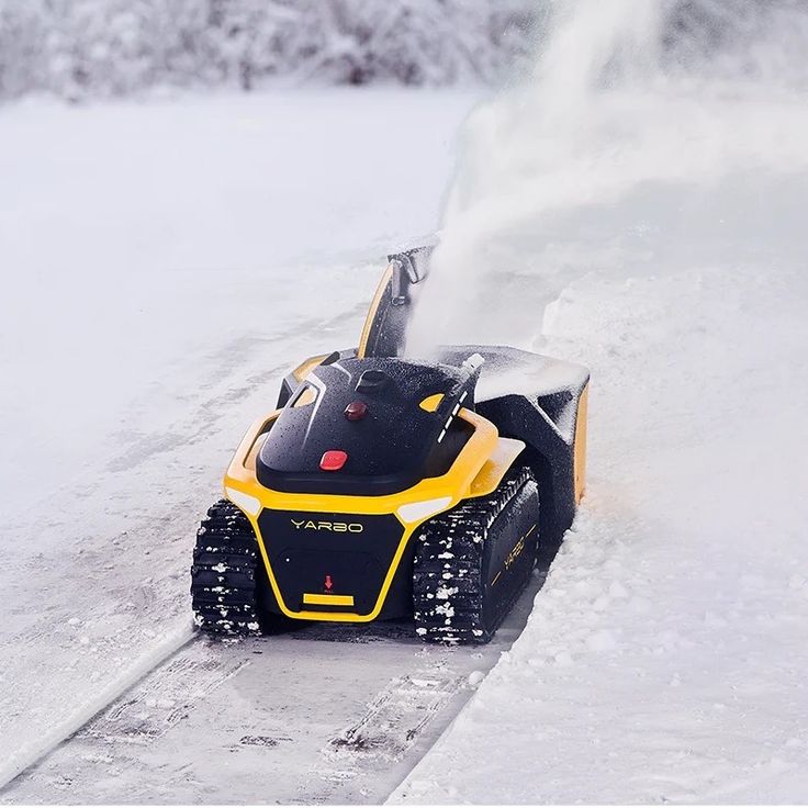 a yellow and black snow blower sitting on the side of a road covered in snow