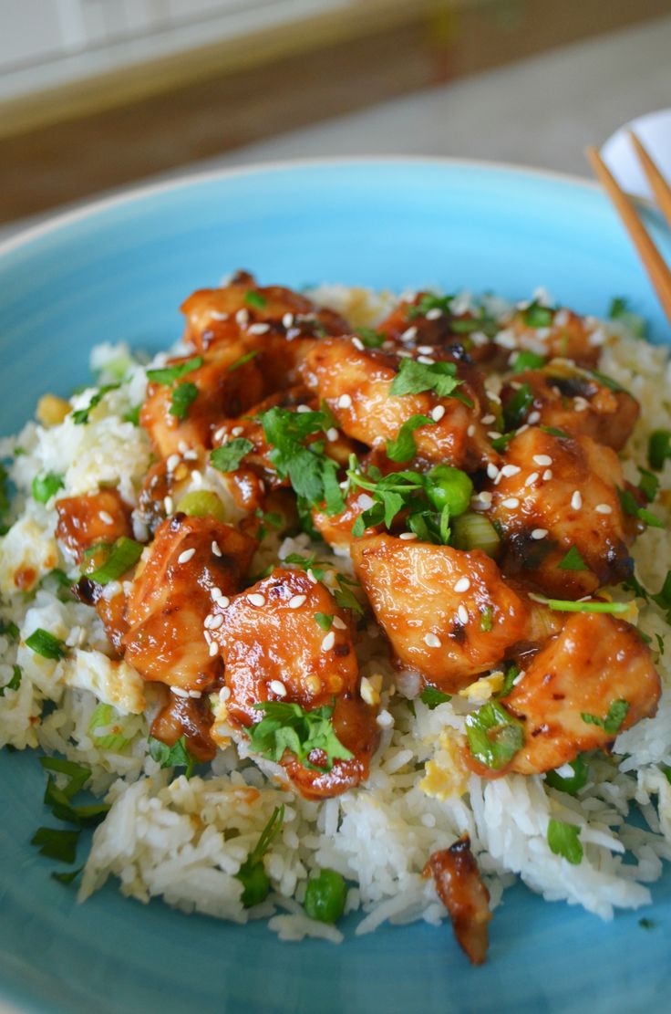 a blue plate topped with rice and chicken on top of green onions next to chopsticks