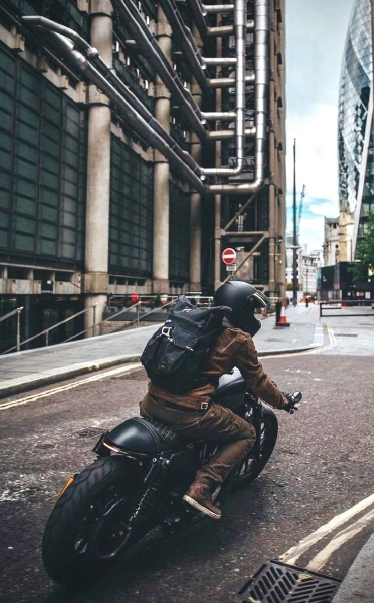 a man riding on the back of a motorcycle down a street next to tall buildings