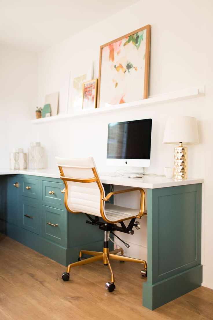 a desk with a computer on top of it in front of a wall mounted painting