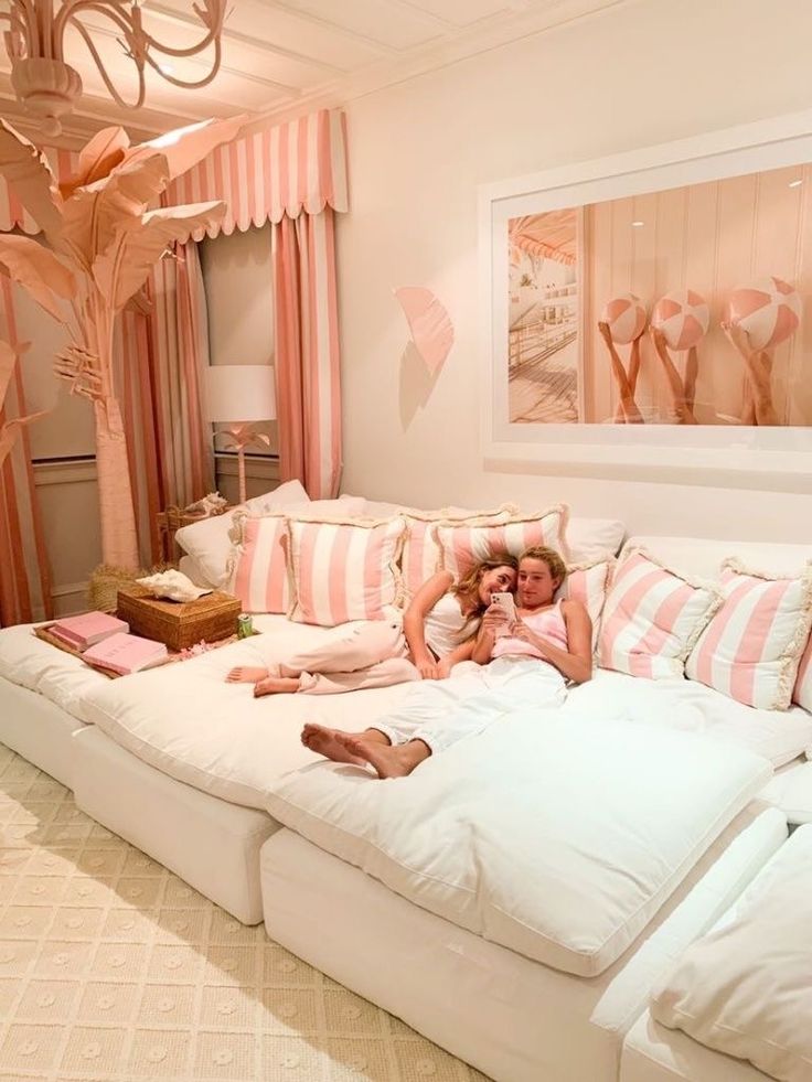 two people laying on a large white couch in a living room with pink and white decor