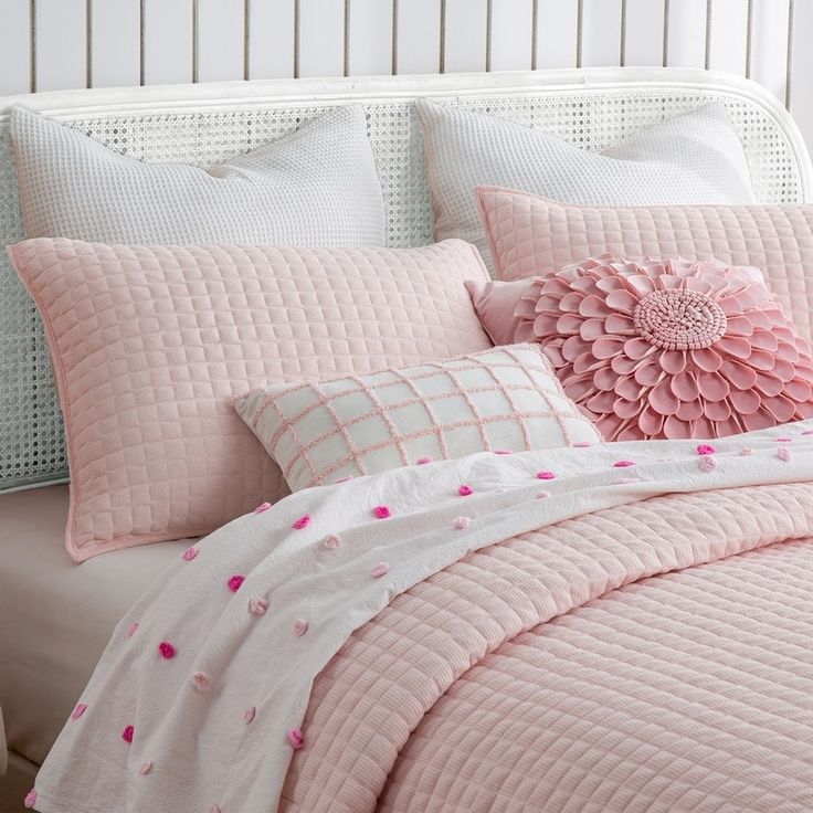 a bed with pink comforters and pillows on top of it, next to a white headboard